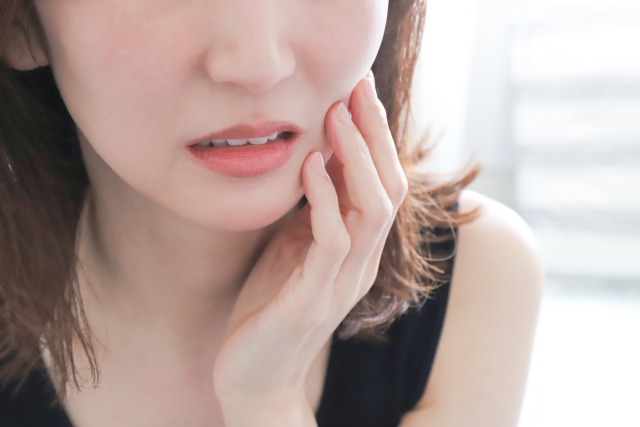歯がしみて頬を押さえる女性